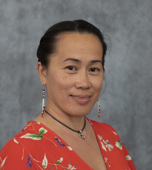 Wendah Alvarez wears a red blouse and is smiling at the camera in front of a grey background.