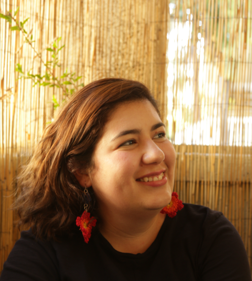 Anna smiles in front of a stringy yellow curtain, with long red earrings hanging from her ears.