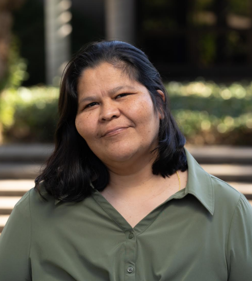 Ana Castellon is pictured in a green long sleeve shirt with a natural background.