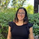 Ana smiles at the camera in front of a natural background.