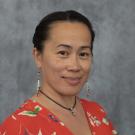 Wendah Alvarez wears a red blouse and is smiling at the camera in front of a grey background.