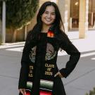 Joy Ok smiles and poses for the camera in a graduate stole.