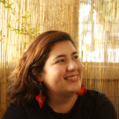 Anna smiles in front of a stringy yellow curtain, with long red earrings hanging from her ears.
